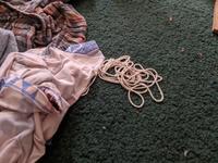 A bundle of string lays on the floor amidst some laundry