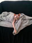 Pearl peeks out of a blanket with one arm outstretched and dangling a comically long distance downwards